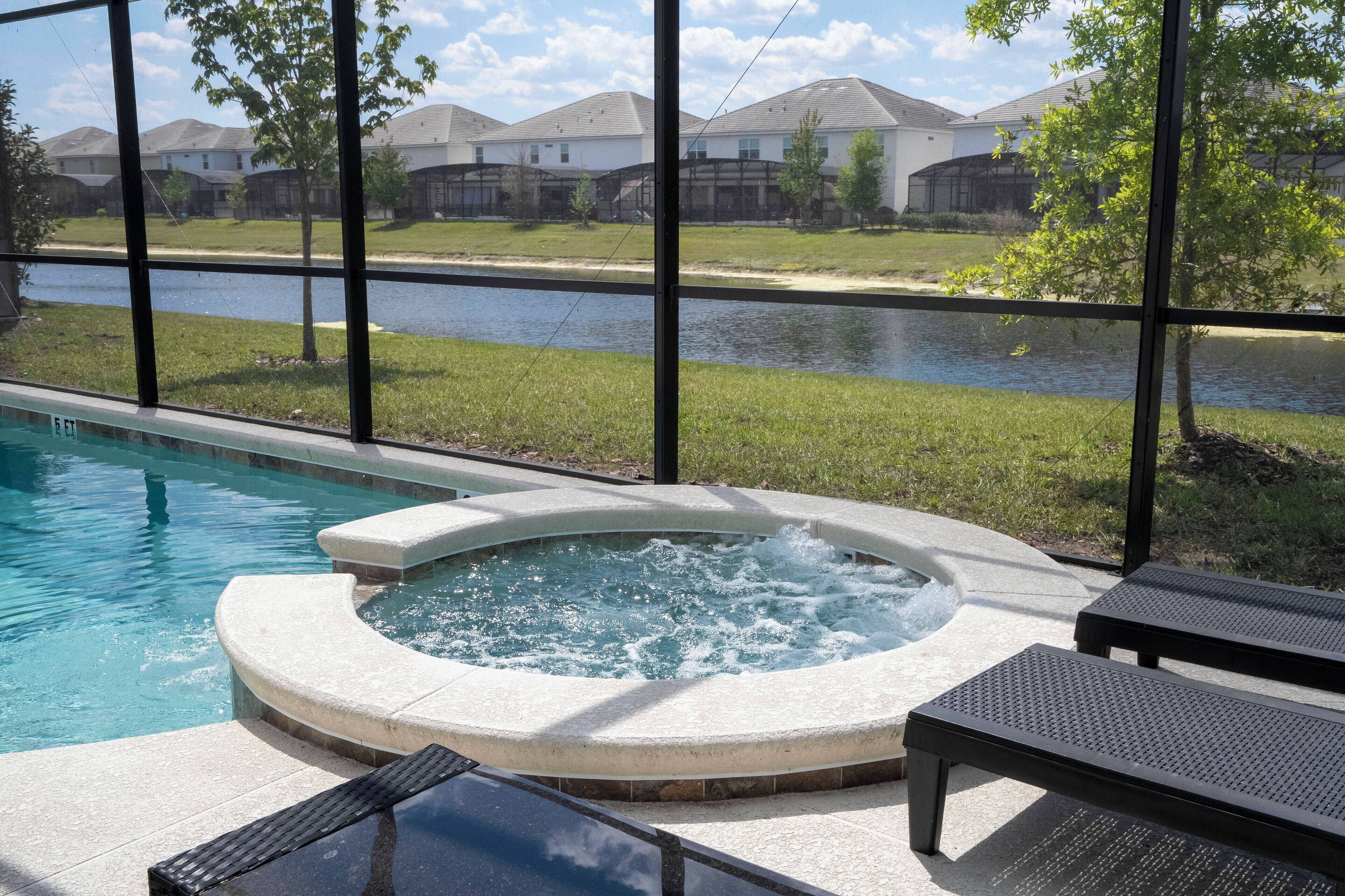 A swimming pool with a hot tub, lounge chairs, and a view of a river and houses in the background.