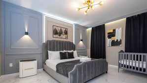 Ein modernes Schlafzimmer mit einem großen Bett, Nachttischen, einem Babybett und Wandleuchten.