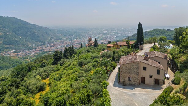 A stone building with a tiled roof, surrounded by lush greenery and a winding road. - Agriturismo La Marginella (Pescia)
