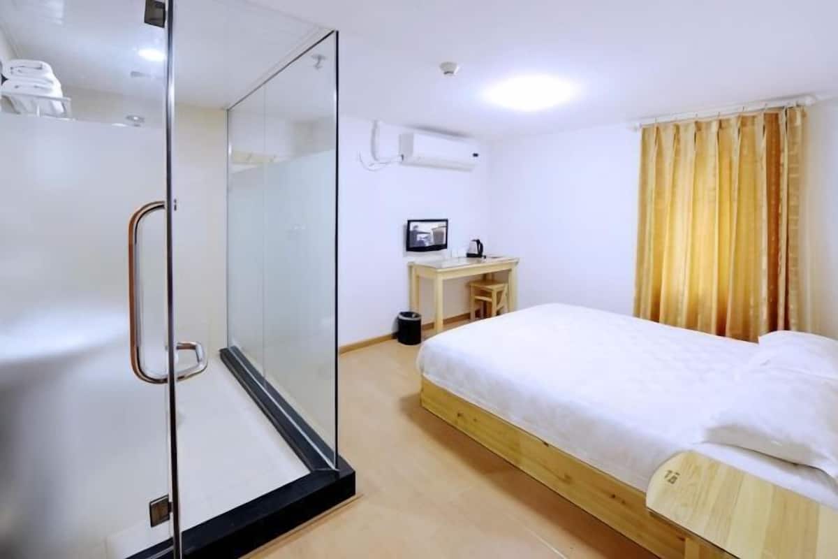A bedroom with a bed, a desk, a chair, a shower, and a window with curtains.