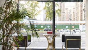A modern interior with a view of a street through large windows, featuring a potted plant, two black chairs, and a small round table. - Golden Inns (Beijing Dajiaoting) (Beijing)