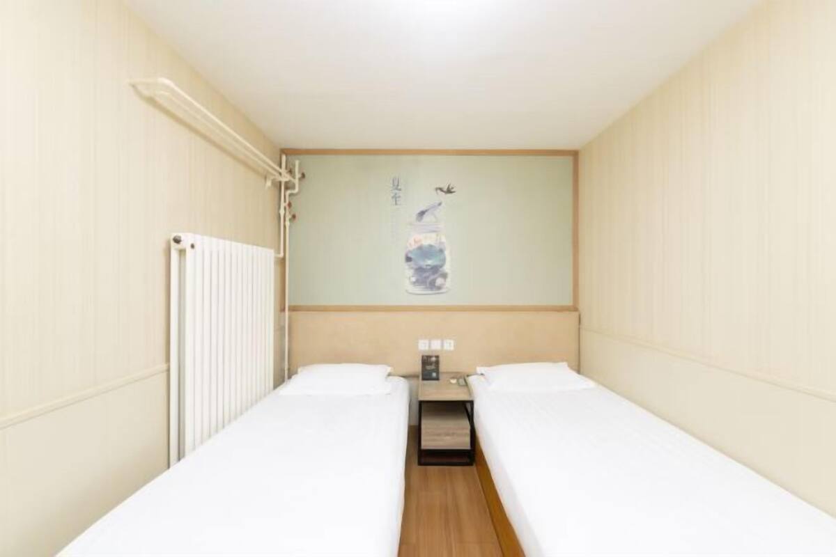 A hotel room with two single beds, a wooden nightstand, and a wall-mounted artwork.