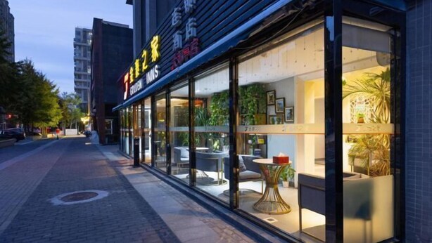A modern hotel with a glass facade, outdoor seating area, and visible interior decor. - Golden Inns (Beijing Dajiaoting) (Beijing)