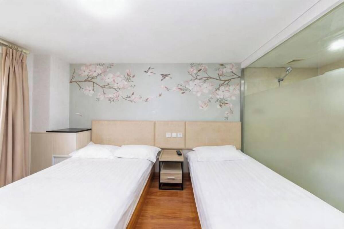 A hotel room with two single beds, a wooden floor, a headboard with a floral mural, and a glass partition on one side.