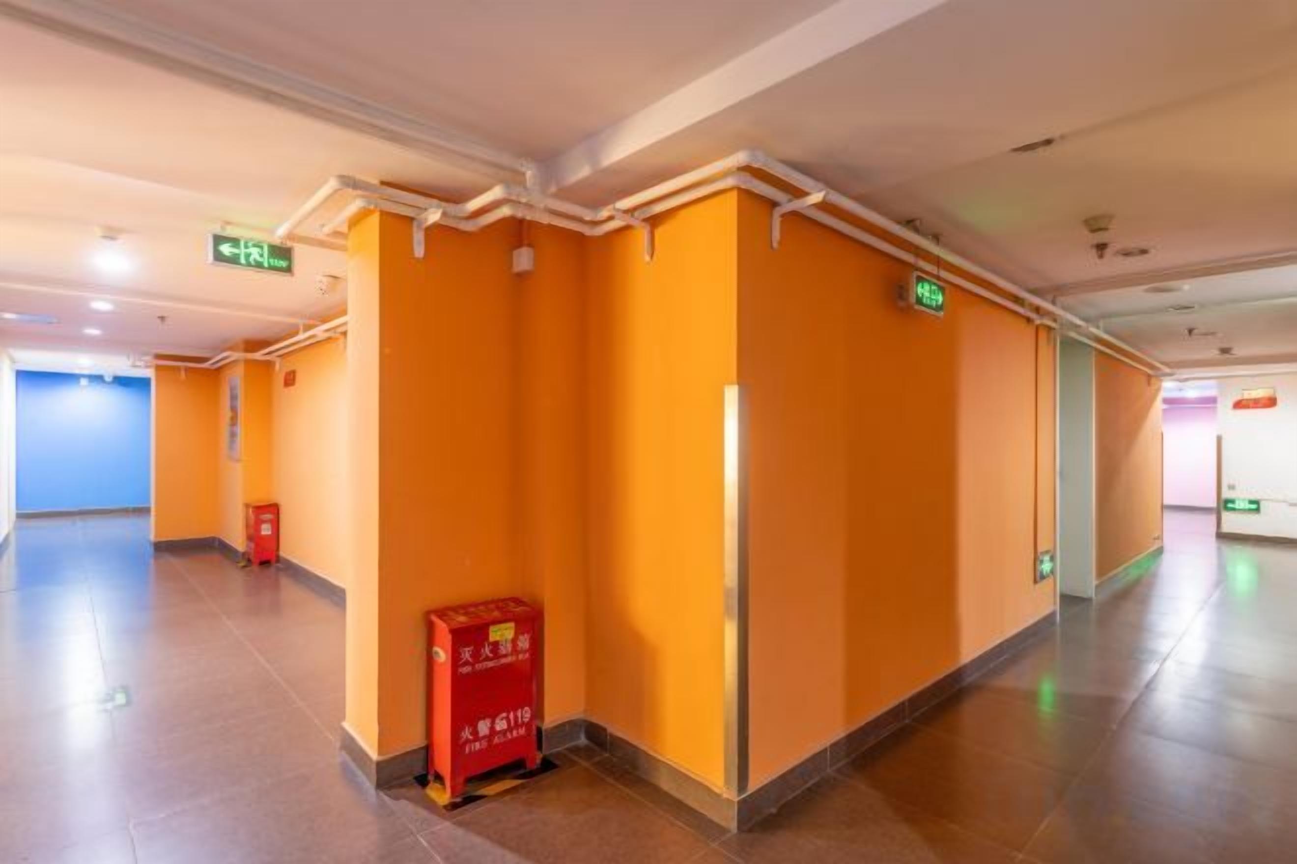 A hotel corridor with orange walls, a red sign, and an emergency exit sign.