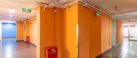 A hotel corridor with orange walls, a red sign, and an emergency exit sign.