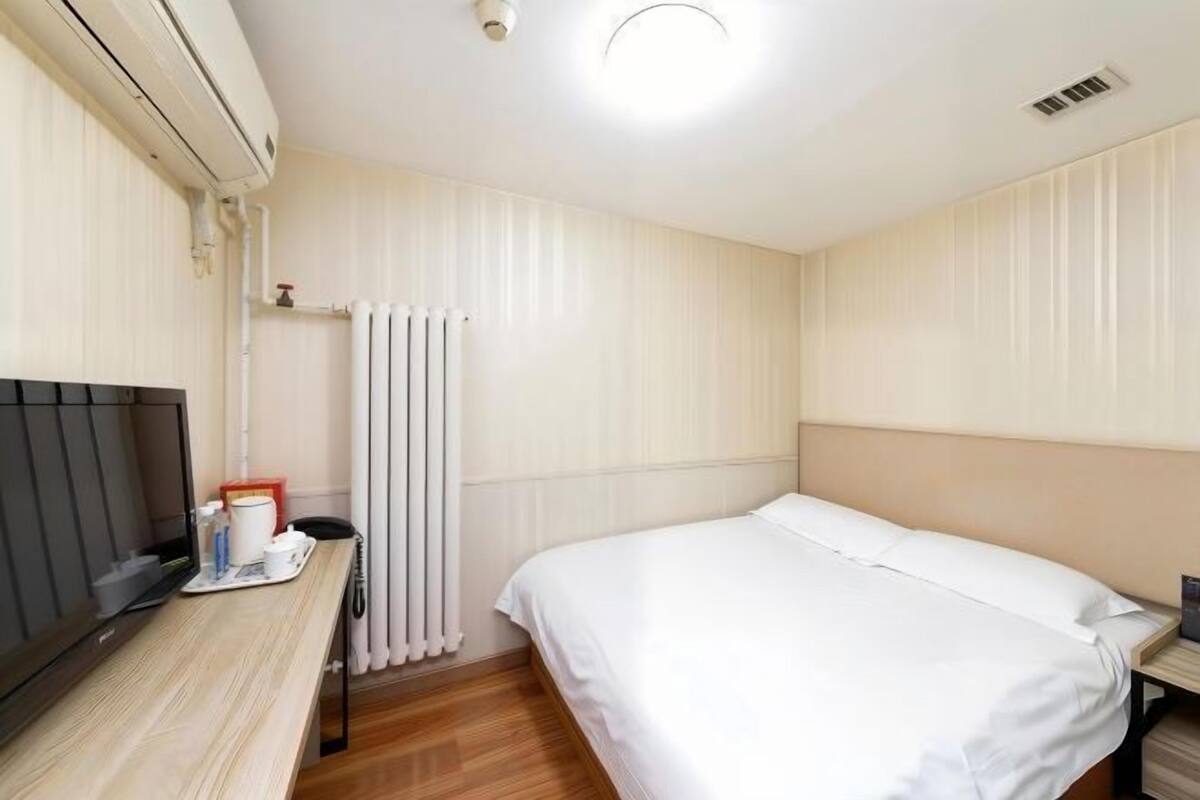 A hotel room with a bed, a TV, a radiator, and a wooden desk.