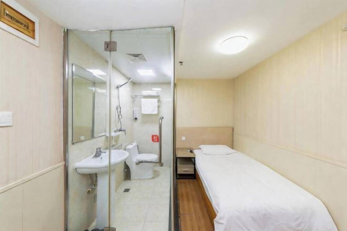 A small, single-room hotel bathroom with a glass shower enclosure, a sink, and a toilet.