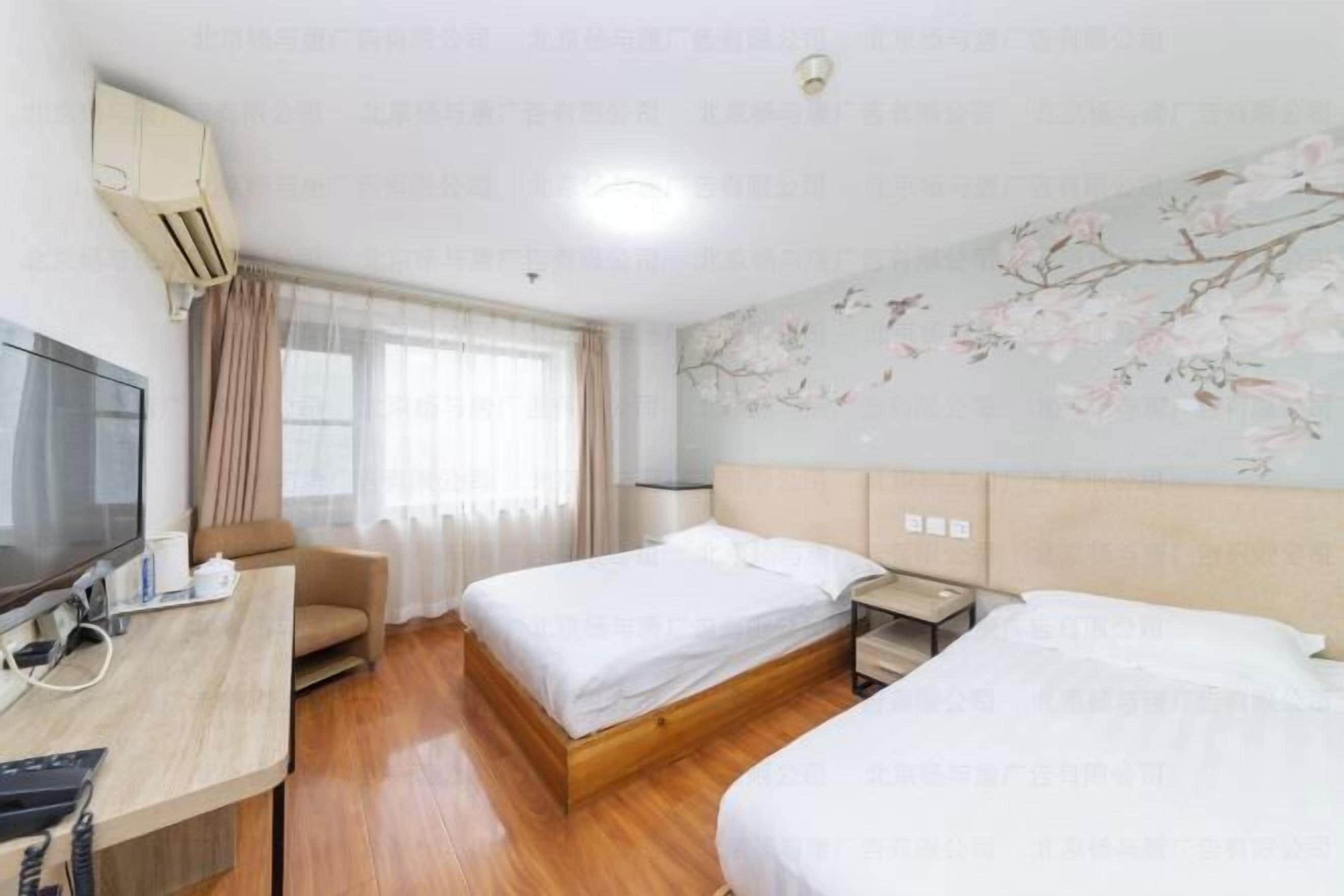 A hotel room with two beds, a desk with a computer, a TV, and a window with curtains.