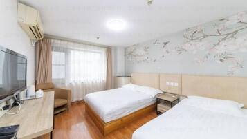 A hotel room with two beds, a desk with a computer, a TV, and a window with curtains.