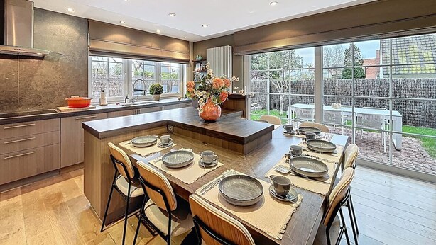 A modern kitchen with a central island, large windows, and a view of the backyard. - Villa Charme - Koksijde (Koksijde)