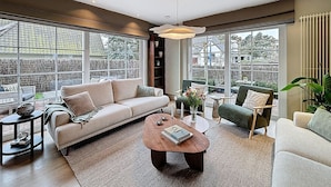 A spacious living room with a large window, a sofa, a coffee table, and a chair. - Villa Charme - Koksijde (Koksijde)