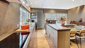 A modern kitchen with a central island, wooden cabinetry, and a large window providing natural light. - Villa Charme - Koksijde (Koksijde)