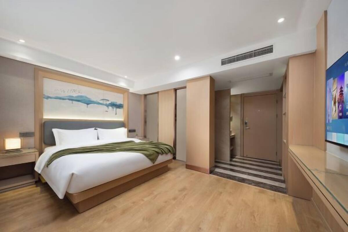 Een moderne hotelkamer met een groot bed, een nachtkastje, een schilderij aan de muur en een televisie aan de rechterkant.