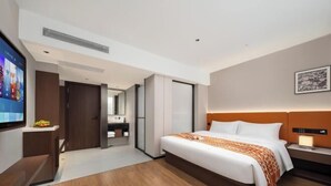 Une chambre d’hôtel moderne, dotée d’un grand lit, d’une télévision, d’un bureau et d’une salle de bain visible à travers une porte ouverte.