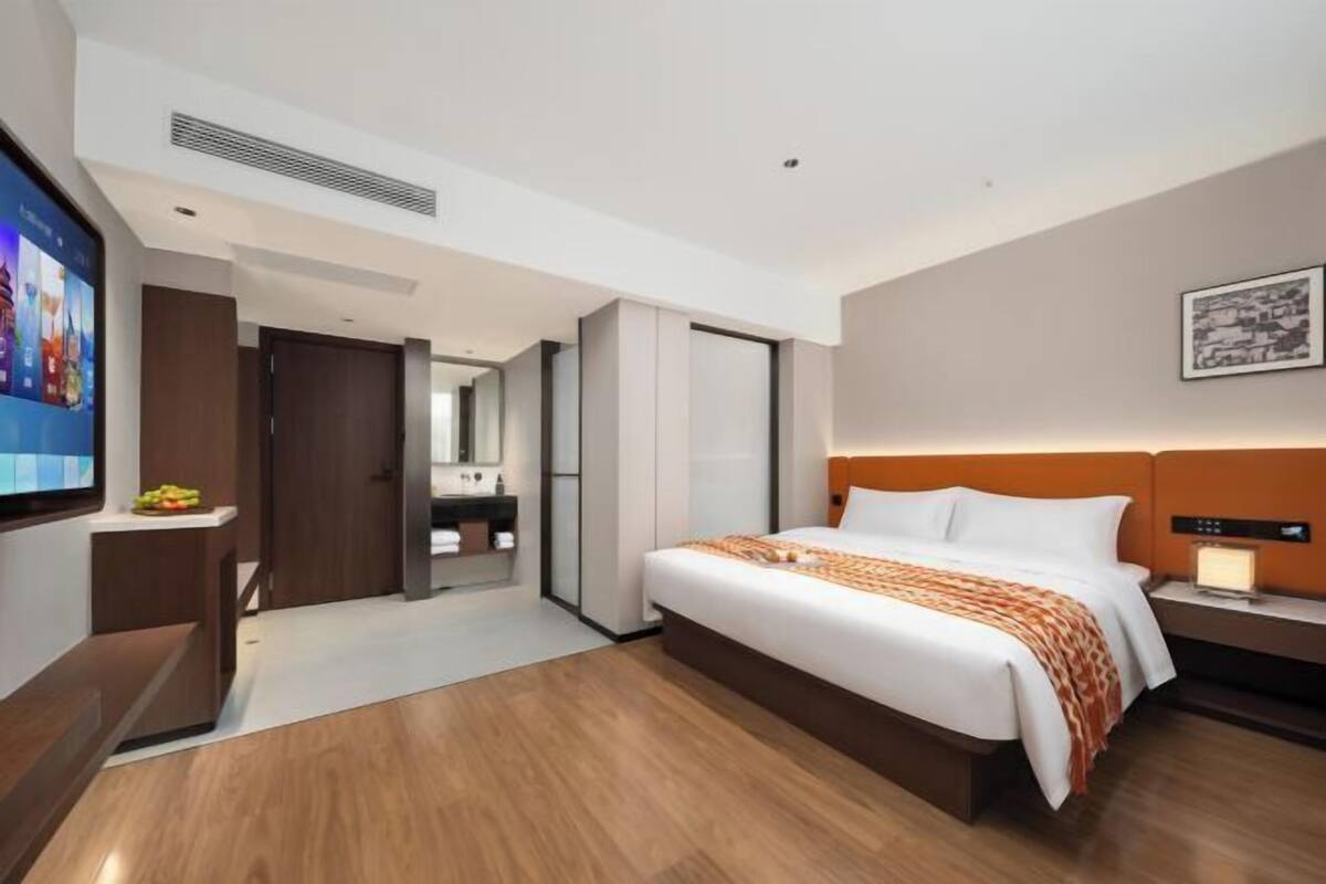 Een moderne hotelkamer met een groot bed, een televisie, een bureau en een badkamer zichtbaar door een geopende deur.