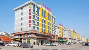 Un hôtel à plusieurs étages, doté d’une façade jaune et blanche bien visible, de nombreux commerces au rez-de-chaussée et surplombant un ciel d’un bleu éclatant.