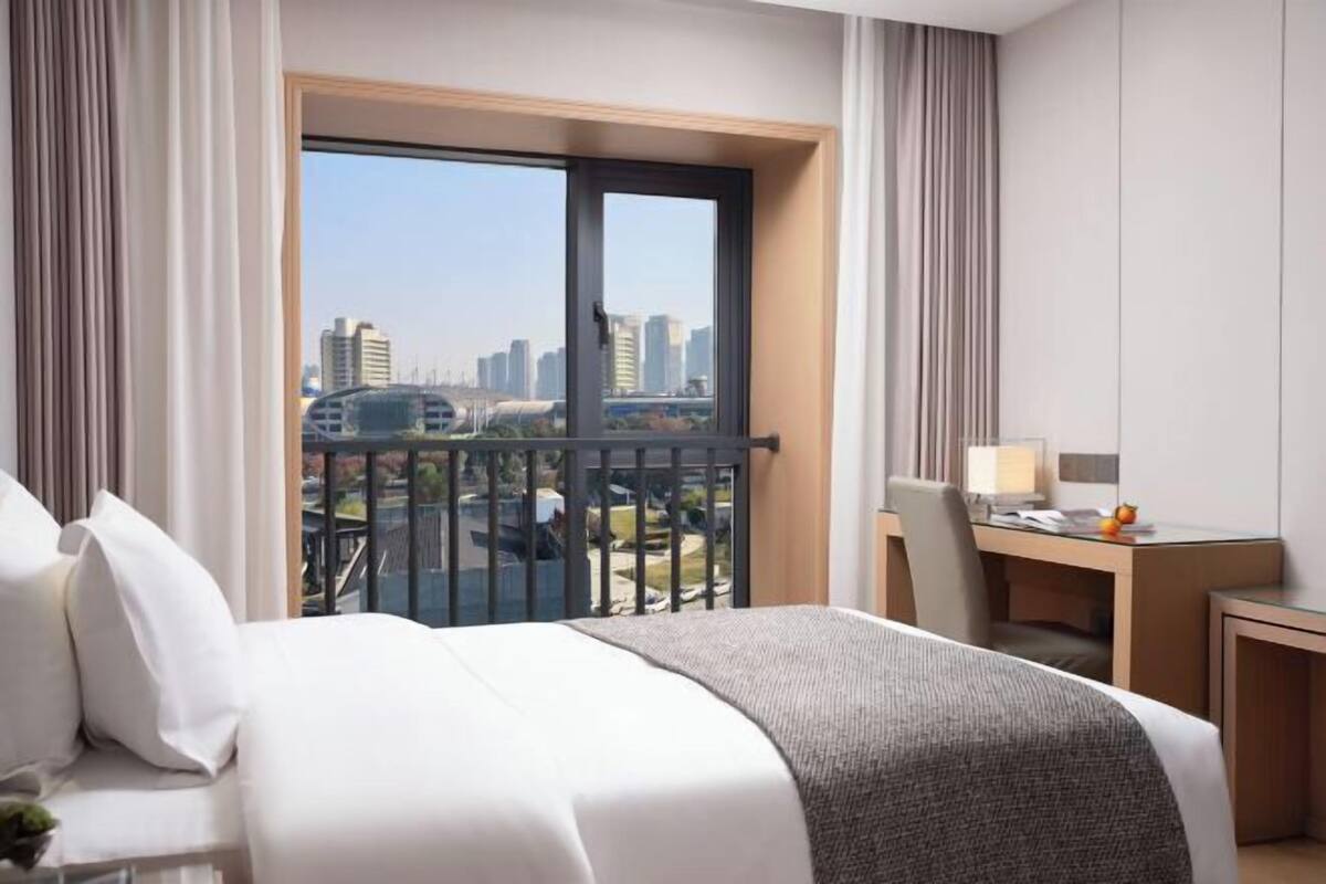 Een hotelkamer met een bed, een bureau en uitzicht op een stadsgezicht door een groot raam.