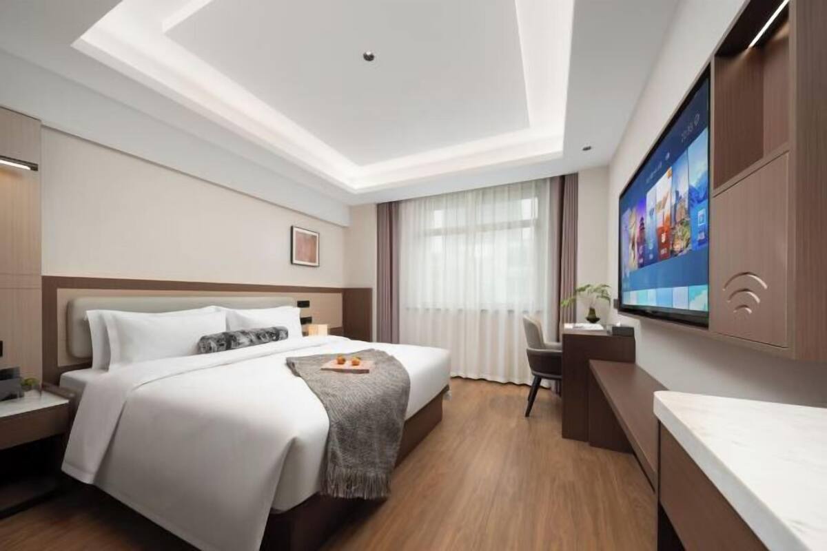 Een moderne hotelkamer met een groot bed, een bureau, een flatscreen televisie en een plafondlamp.