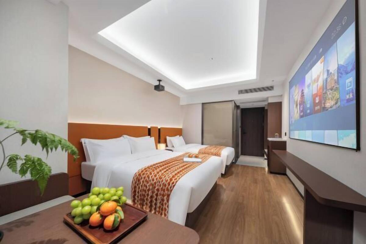 Een hotelkamer met twee bedden, een eettafel met fruit, een groot raam en een tv aan de muur.