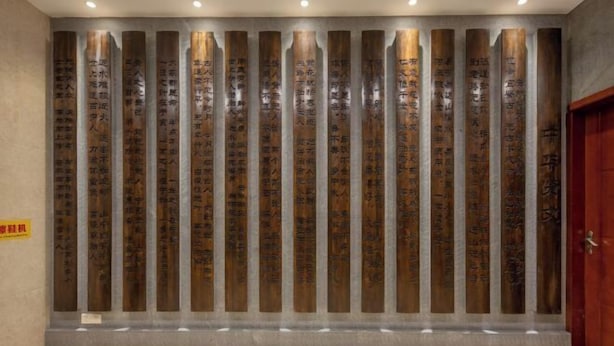 Un mur orné de panneaux de bois verticaux portant des inscriptions, un sol en marbre et une porte en bois.