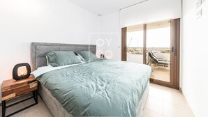 Un dormitorio moderno con una cama grande, una mesita de noche y vistas al exterior por una puerta corredera.
