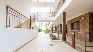 Un pasillo con piso de baldosas, barandillas de metal y una escalera que lleva a un nivel superior.