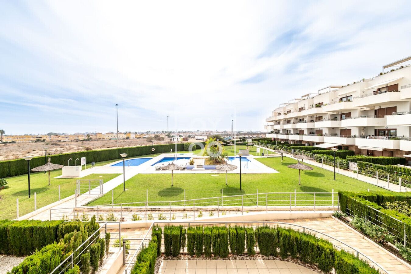 Een modern appartementencomplex met een centrale binnenplaats, inclusief een zwembad, omringd door verzorgde gazons en hagen.