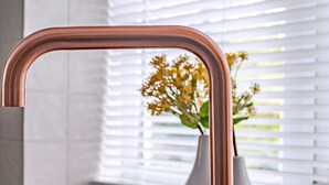 A kitchen sink with a copper faucet and a vase with flowers on the windowsill. - Spacious modern apartment in South Croydon (South Croydon)