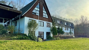 A modern building with a prominent triangular roof, large windows, and a well-maintained lawn. - Barbarossa Hotel Kelbra (Kelbra)