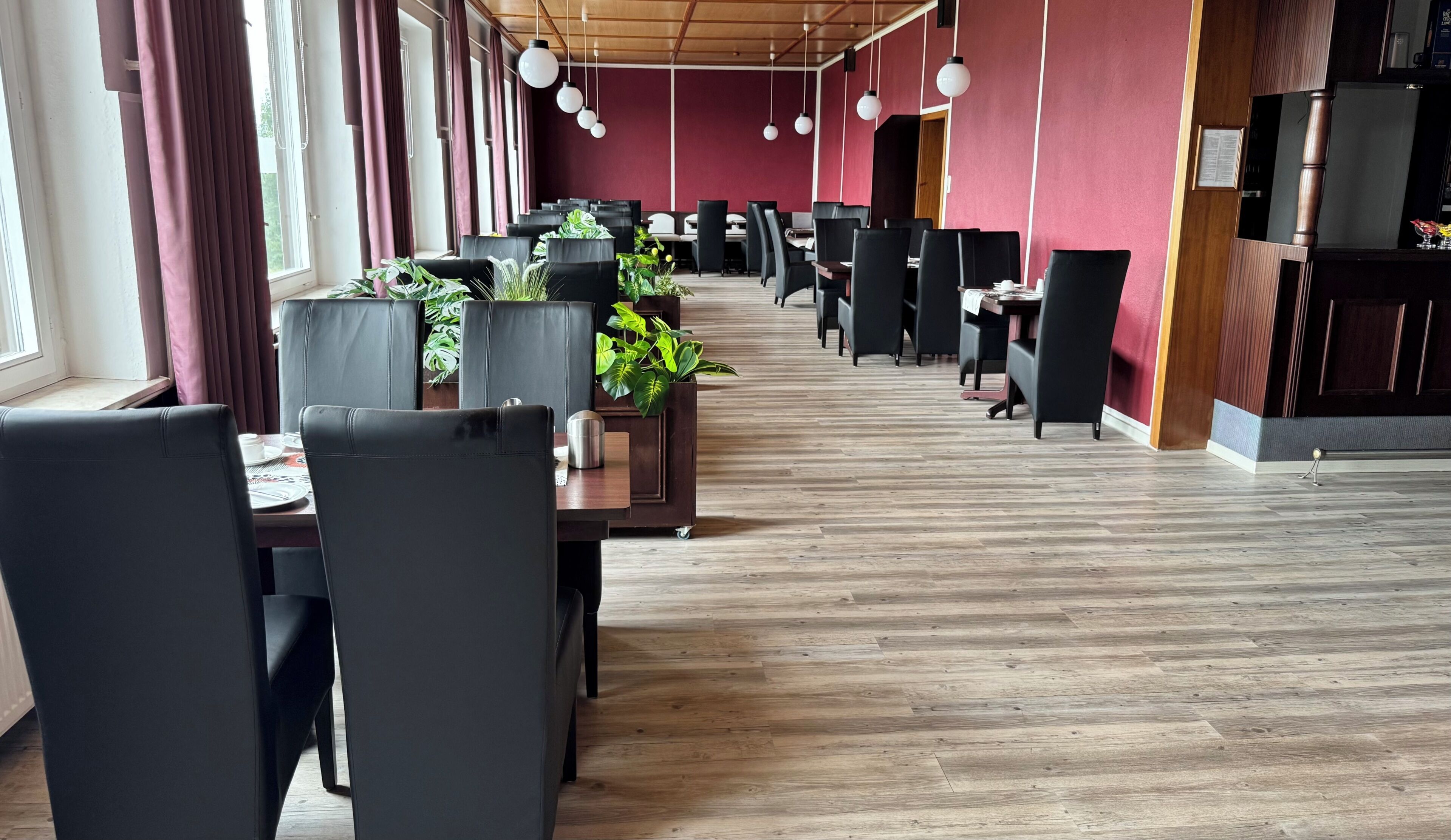A modern restaurant with black leather chairs, wooden tables, and potted plants.