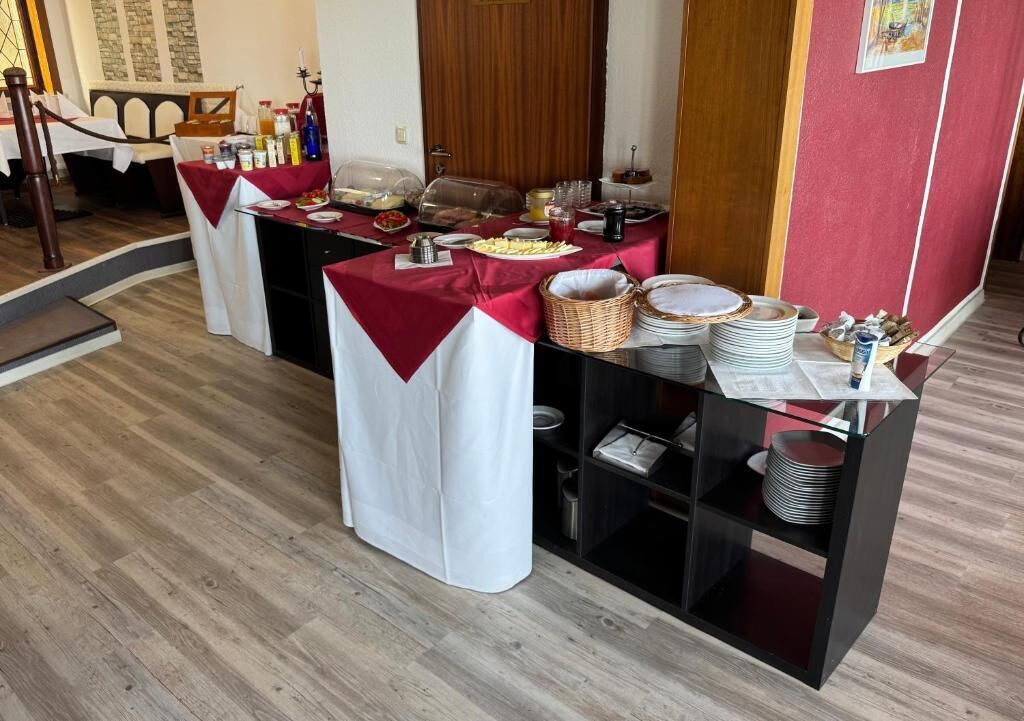 Ein Buffet mit abgedeckten Speiseausgaben, einem Büfett mit roter Tischdecke und einer Anrichte mit gestapelten Tellern und Körben.