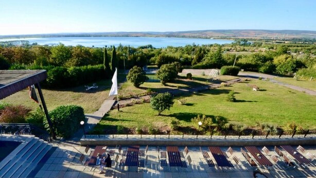 A terrace with outdoor seating and a view of a lake and distant hills. - Barbarossa Hotel Kelbra (Kelbra)