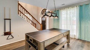 A ping pong table in a room with wooden flooring, a staircase, and a door. - Comfortable 5BR 3BA • Central Location (Rowlett)