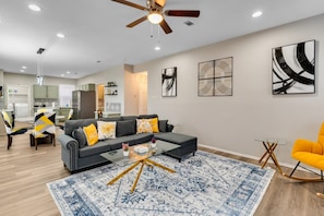 A modern living room with a grey sofa, yellow cushions, a glass coffee table, and a blue patterned rug. - Comfortable 5BR 3BA • Central Location (Rowlett)