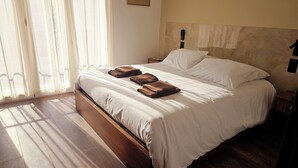 Ein ordentlich bezogenes Bett mit weißen Leinentüchern und drei gefalteten braunen Handtüchern.