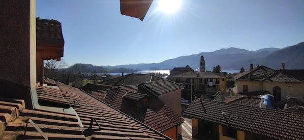 A view of a town with terracotta-roofed buildings, a church with a bell tower, and a lake in the background.