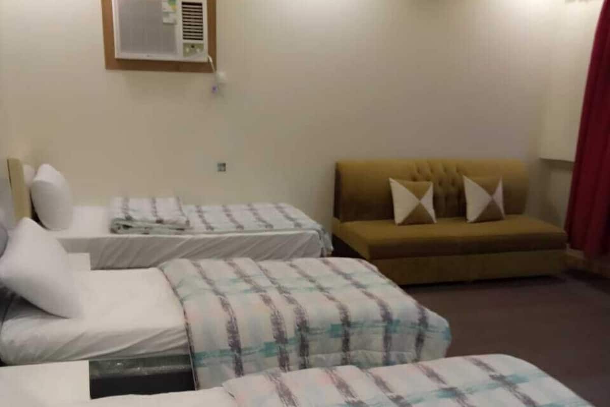 A hotel room with two beds, a sofa, an air conditioning unit, and a red curtain.