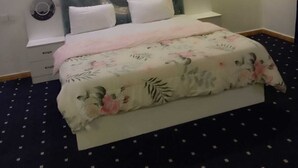Un dormitorio con cama, mesita de noche, ventilador de pared y luz de techo.