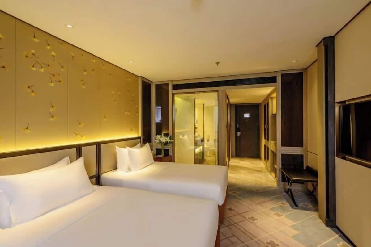 Een hotelkamer met twee bedden, een grote spiegel, een bankje en een gang naar een andere kamer.