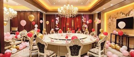 A round table with chairs, a chandelier, and red and gold balloons.
