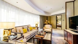 Ein Hotelzimmer mit Sofa, Sessel, Couchtisch, Fernseher und einem großen Fenster mit Vorhängen.