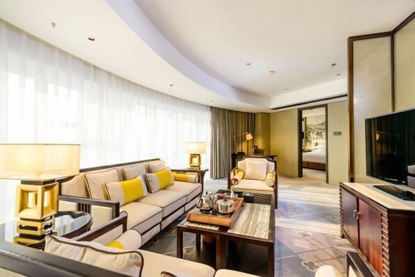 A hotel room with a sofa, armchair, coffee table, TV, and a large window with curtains. - Dahe Jinjiang Hotel (Zhengzhou)