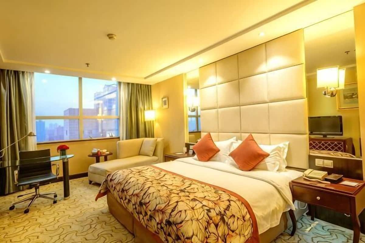Een hotelkamer met een groot bed, een bureau, een stoel, een televisie en uitzicht op de stad.