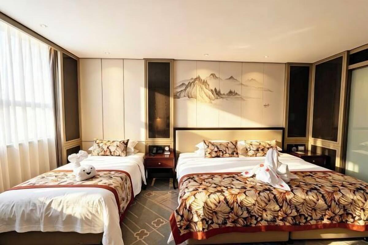 Een hotelkamer met twee bedden, een groot schilderij aan de muur en een raam met gordijnen.