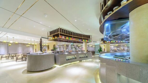 Un hall d’hôtel moderne doté d’un comptoir d’accueil central, d’espaces détente et d’un plafond haut avec des poutres apparentes.