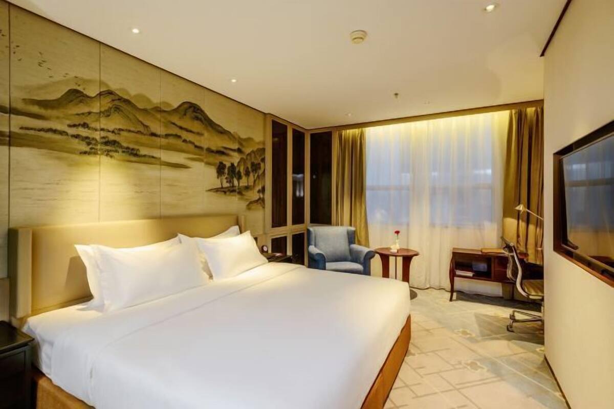 Een hotelkamer met een groot bed, een bureau, een stoel, een televisie en een muur met een schilderij.