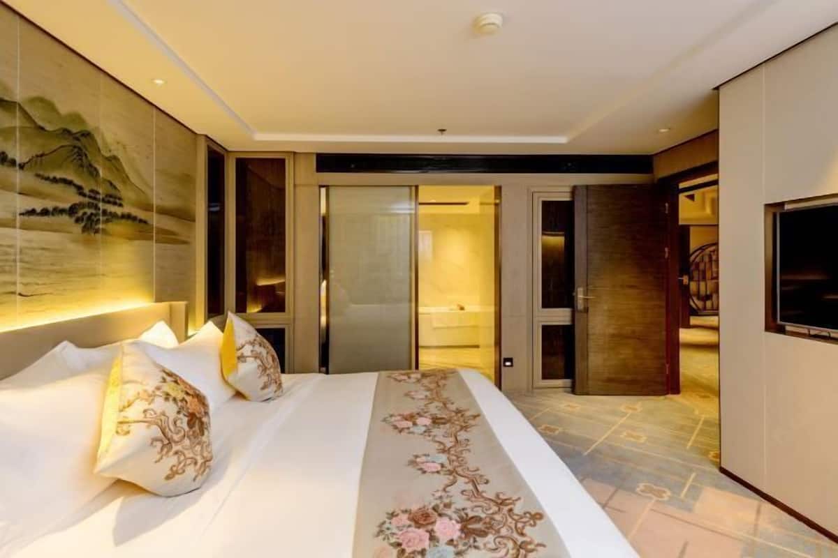 Hotelkamer met een groot bed, een schilderij aan de muur en een schuifdeur naar een badkamer.