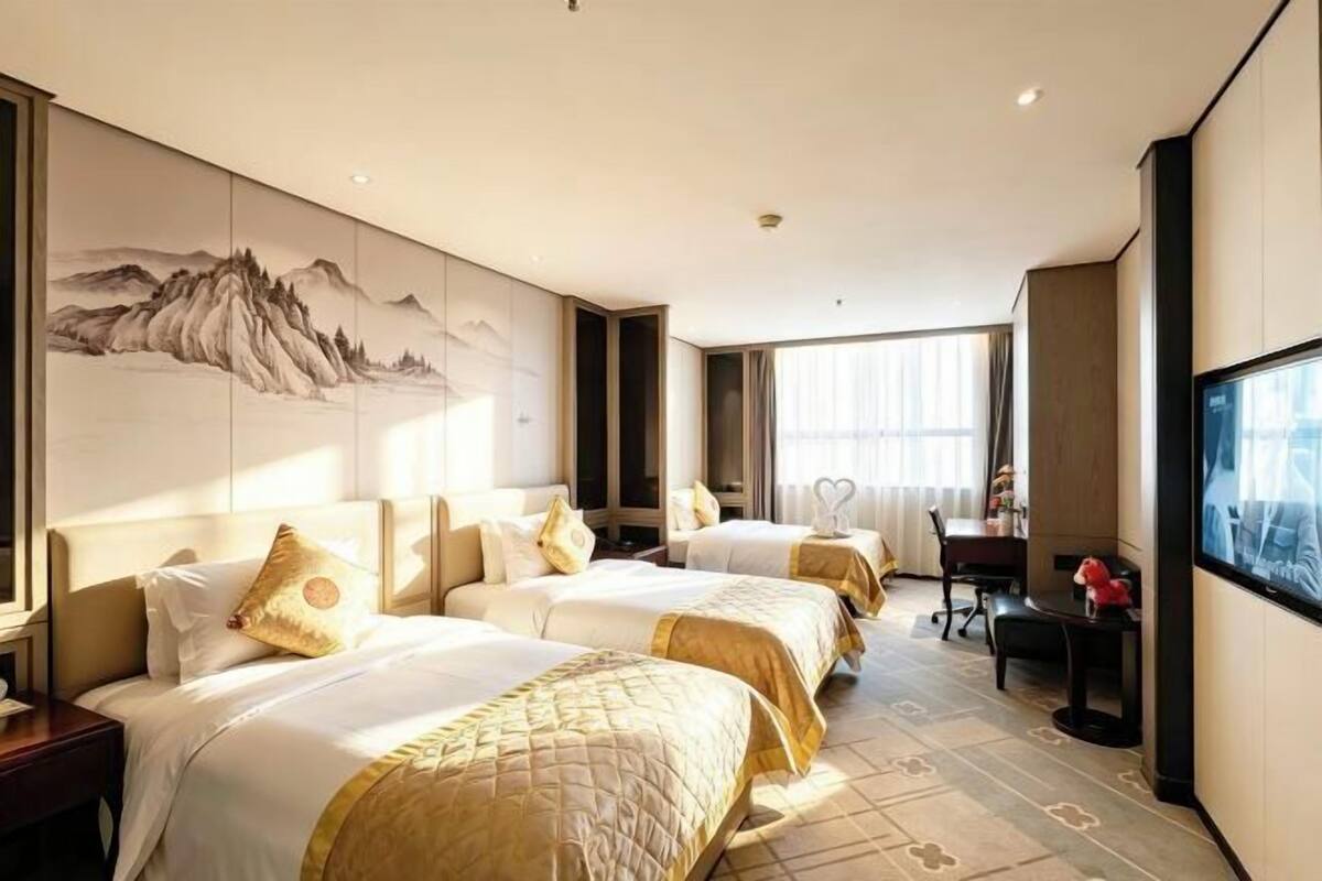 Een hotelkamer met drie bedden, een bureau, een stoel en een groot televisiescherm.