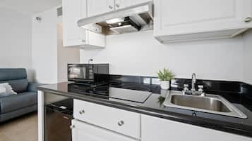 A compact kitchen with white cabinets, a black countertop, a built-in microwave, a stainless steel sink, and a compact dishwasher.